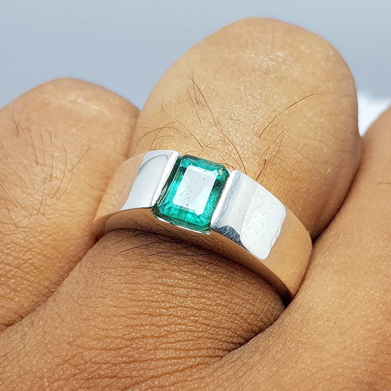 May include: A silver ring with a square emerald green gemstone set in the center.
