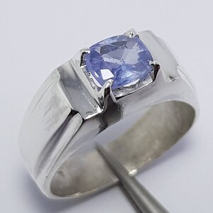 May include: A silver ring featuring a light blue gemstone set in the centre. The ring has a simple, classic design.