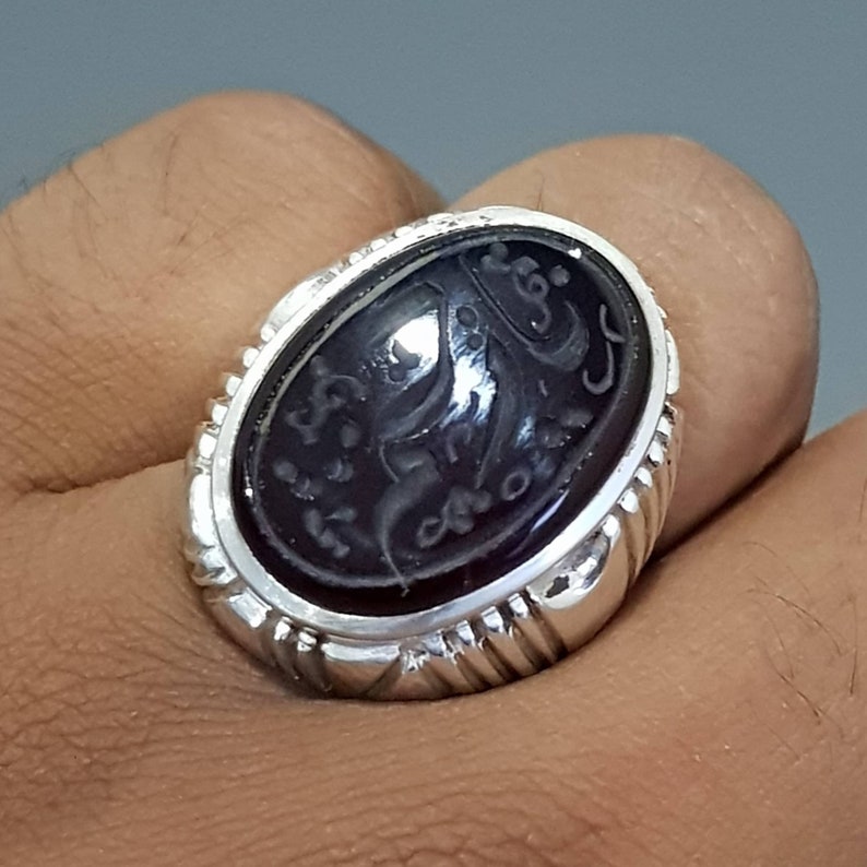 May include: A silver ring with a black oval gemstone featuring intricate engraved Arabic script.