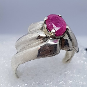 May include: A silver ring featuring a pink ruby gemstone set in the centre. The ring has a distinctive, wavy design.