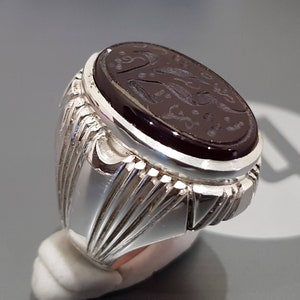 May include: A silver ring with an oval-shaped black onyx stone set in the center. The stone has intricate carvings and a silver band with a detailed design.
