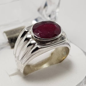 Può includere: Un anello d'argento con una pietra ovale di colore rosso intenso incastonata in una montatura a castone. La fascia dell'anello ha un design testurizzato.