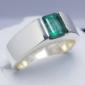 May include: A silver ring with a green emerald gemstone set in a square shape.