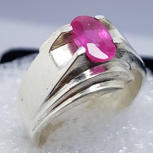 May include: A silver ring with a pink oval gemstone set in the center. The ring has a textured band with three raised lines.