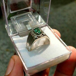 May include: A silver ring with a green gemstone set in a decorative band.