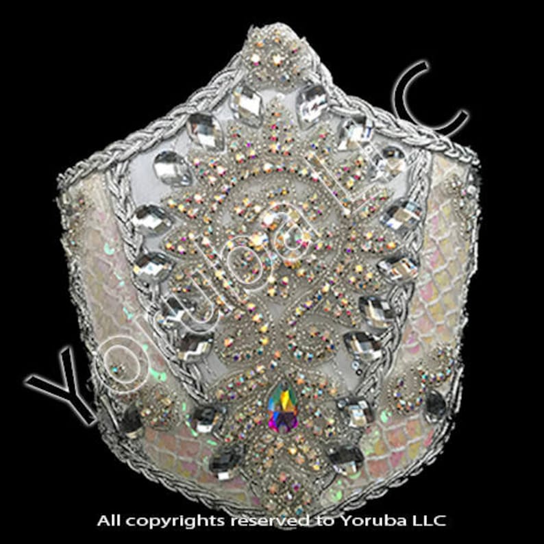 Puede incluir: Una corona blanca con un dise&ntilde;o de cuentas plateadas y diamantes de imitaci&oacute;n iridiscentes. La corona est&aacute; decorada con un gran patr&oacute;n floral adornado.