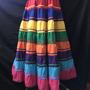 May include: A colourful, multi-tiered skirt with a brown waistband. The skirt is made of different coloured fabrics, including red, yellow, green, blue, and purple. Each tier is separated by a contrasting coloured trim.