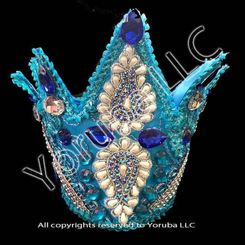 Puede incluir: Una corona azul con adornos blancos y azules y diamantes de imitaci&oacute;n azules. La corona est&aacute; hecha de tela y tiene una punta puntiaguda.