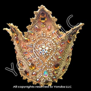 Puede incluir: Una corona dorada con una parte superior puntiaguda y detalles intrincados. La corona est&aacute; decorada con diamantes de imitaci&oacute;n y joyas de color &aacute;mbar.