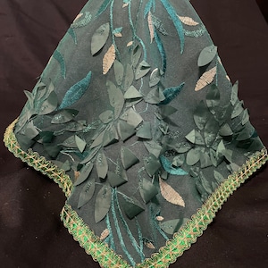 May include: A green lace fabric with a floral design. The fabric has a gold trim around the edges.