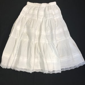 Peut inclure: Une jupe blanche à volants avec une bordure en dentelle. La jupe a une taille élastiquée et une silhouette fluide.