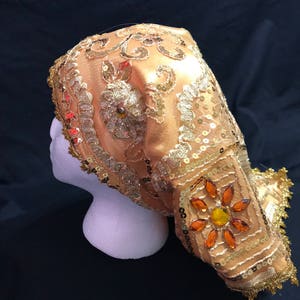 May include: A gold and orange sequined head covering with a floral design. The head covering is made of a soft, sheer fabric and is decorated with gold and orange sequins and beads.