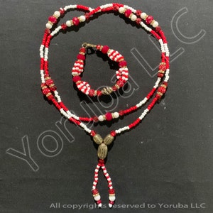 May include: A red and white beaded necklace and bracelet set with a gold pendant. The necklace has a tassel at the bottom.