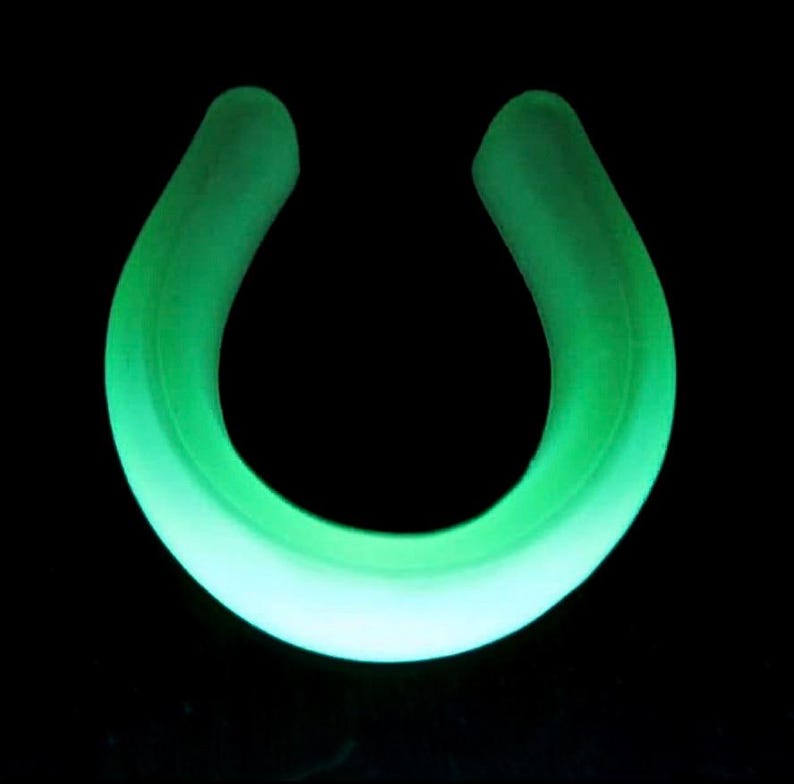 May include: A glowing green, horseshoe-shaped object against a black background. The object has a smooth, rounded form, with a gradient of color from a bright, almost white center to a darker green edge.