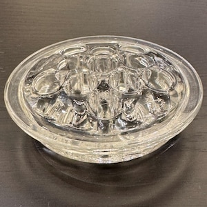 May include: Clear glass flower frog with multiple holes for arranging stems. The round frog has a shallow base and is designed to hold flowers in place. The glass is transparent, allowing the water to be visible.