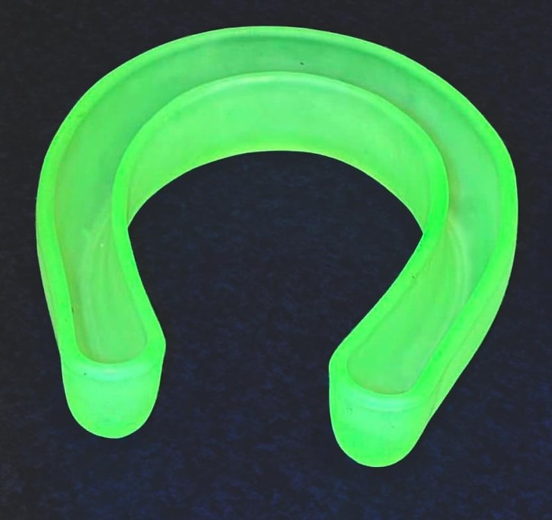 May include: A neon green, U-shaped object with a rounded design. The object appears to be made of a translucent material, with a smooth, curved surface. The object is set against a dark background.