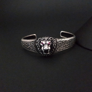May include: Silver bracelet with a lion head design. The lion's eyes are set with pink gemstones.