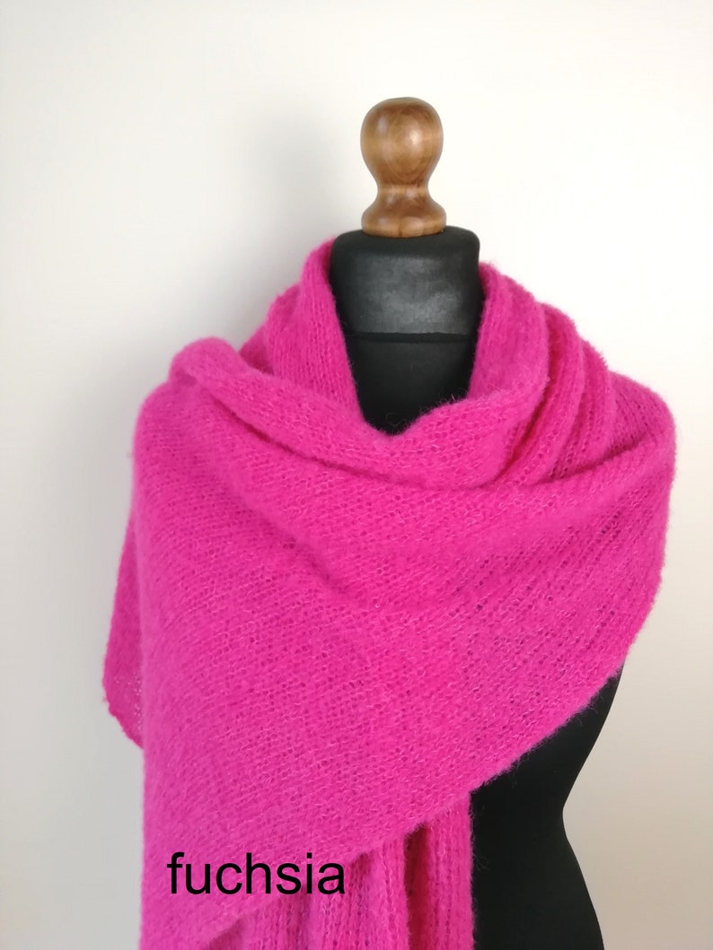 May include: A fuchsia-colored scarf draped over a mannequin. The scarf is made of a soft, fuzzy material and is wrapped around the mannequin's neck and shoulders. The word "fuchsia" is printed on the scarf.