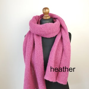 May include: A heather pink scarf displayed on a black mannequin. The scarf is made of a soft, knitted material and is draped to showcase its length and texture. The word "heather" is printed on the scarf.