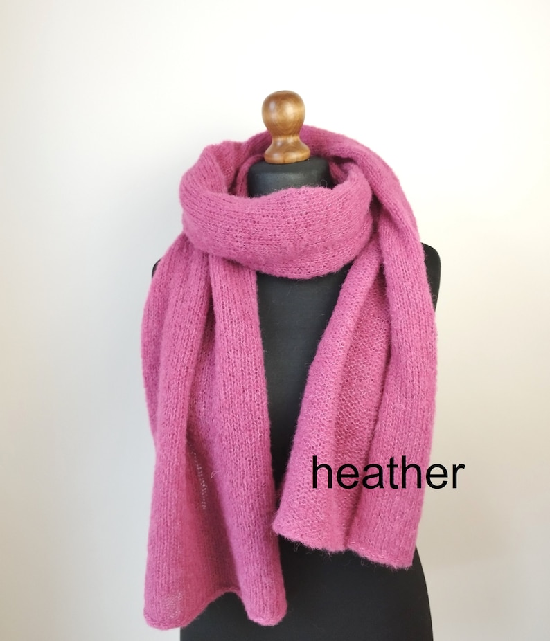 May include: A heather pink scarf displayed on a black mannequin. The scarf is made of a soft, knitted material and is draped to showcase its length and texture. The word "heather" is printed on the scarf.