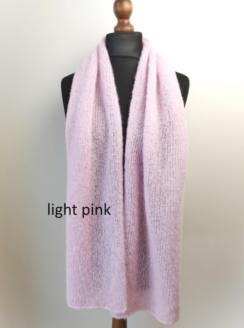 May include: A light pink scarf displayed on a black mannequin. The scarf is made of a soft, knitted material. The text "light pink" is visible on the bottom left of the image. The scarf is a solid color and appears to be a winter accessory.