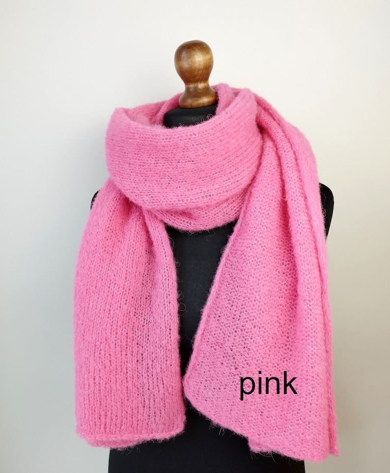 May include: A bright pink, fluffy scarf draped over a mannequin. The scarf is made of a soft, textured material and is a vibrant shade of pink. The word "pink" is written on the scarf in black text.
