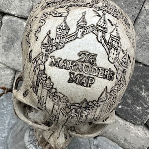 May include: A white ceramic skull with a detailed map of Hogwarts engraved on the top. The map is labeled "The Marauder's Map".