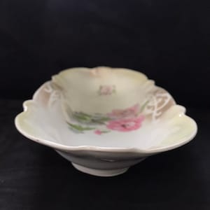 May include: A white porcelain serving dish with a scalloped edge and a floral design. The dish has a light yellow glaze and features pink and green flowers.