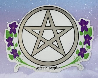 Puede incluir: Una pegatina plateada con un pentagrama y un borde floral de flores moradas y hojas verdes. La pegatina tiene el texto "satanic sapphic" en la parte inferior.