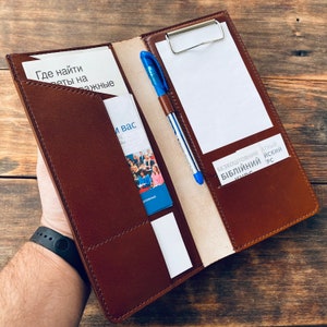 May include: A brown leather folder with multiple pockets and a built-in clipboard. The folder has a white card with the text "Где найти ответы на важные вопросы" and a blue pen.