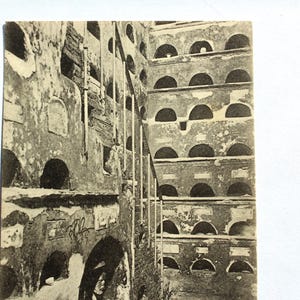 May include: Black and white photo of a building with many arched windows. The building is made of stone and has a weathered look. The photo is taken from a low angle, looking up at the building.