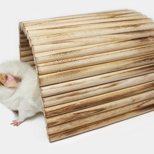 May include: A white and brown guinea pig peeks out of a wooden tunnel toy. The tunnel is made of natural wood slats and is a great enrichment item for small pets.