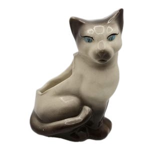 Può includere: Fioriera a forma di gatto siamese in ceramica. Il gatto ha un corpo beige chiaro con dettagli marroni scuri sulle orecchie, sulla coda e sulle zampe. Ha occhi blu e un'apertura per piantare.