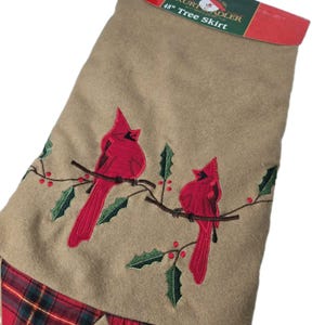 Puede incluir: Falda de árbol de Navidad de color beige con cardenales rojos bordados posados en una rama con hojas de acebo verdes. La falda tiene un borde a cuadros rojo y verde. La etiqueta dice "48" Tree Skirt".