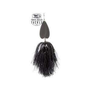 May include: Black fishing lure with a black feather skirt and two silver blades. The lure has a silver hook and a gold ring. The lure is labelled "Tooth Shield Tackle".