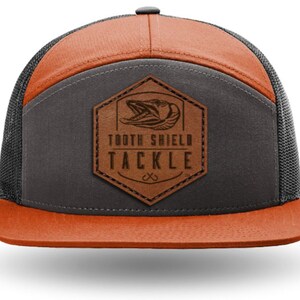 Könnte beinhalten: Eine braune und orangefarbene Trucker-Kappe mit einem braunen Leder-Patch, auf dem "Tooth Shield Tackle" steht und ein Fisch-Motiv abgebildet ist.