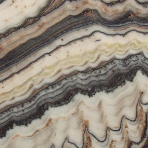 May include: A rectangular slab of layered stone with a natural, uneven edge. The stone features bands of white, cream, gray, and brown, creating a wavy, textured pattern. The colors and patterns suggest a geological formation.