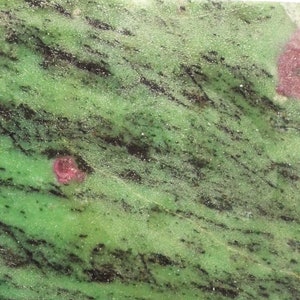 Könnte beinhalten: Ein grüner und schwarzer Stein mit rosa Einschlüssen. Der Stein hat eine raue, natürliche Textur.