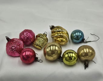 Pode incluir: Uma coleção de nove ornamentos de vidro vintage de várias formas e cores, incluindo esferas cor-de-rosa texturizadas, um ornamento dourado em forma de cesto, uma espiral dourada, uma esfera azul e várias esferas metálicas douradas e amarelas.