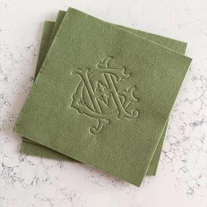 May include: Three olive green square cloth napkins stacked on a white surface. Each napkin features an embossed monogram design in a matching olive green color. The monogram appears to be the letters "A" and "C" intertwined.