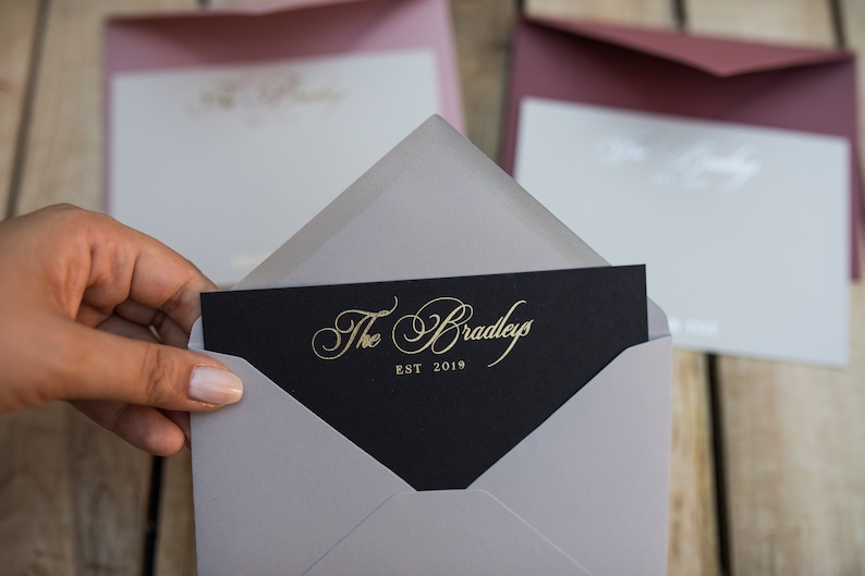 May include: A gray envelope with a black card inside. The card has gold lettering that reads "The Bradleys EST 2019".