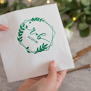 Pu&ograve; includere: Tovagliolo di carta bianco con una cornice geometrica verde e rami con foglie che circondano le iniziali "R & B" e la data "10/27/18".