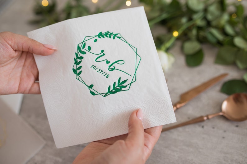 Pu&ograve; includere: Tovagliolo di carta bianco con una cornice geometrica verde e rami con foglie che circondano le iniziali "R & B" e la data "10/27/18".