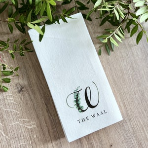 Pode incluir: Toalha de chá de linho branco com um design de folhas de eucalipto verdes e o texto "THE WAAL" impresso em preto.