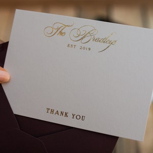 May include: A white thank you card with gold foil lettering. The card says "The Bradley" and "EST 2019" in a script font. The bottom of the card says "Thank You" in a simple font.