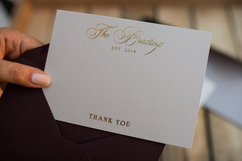 May include: A white thank you card with gold foil lettering. The card says "The Bradley" and "EST 2019" in a script font. The bottom of the card says "Thank You" in a simple font.