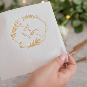 Pu&ograve; includere: Tovagliolo di carta bianco con una cornice geometrica dorata e un motivo floreale. Il testo "r & b 10/27/18" &egrave; stampato all'interno della cornice.