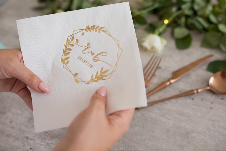 Pu&ograve; includere: Tovagliolo di carta bianco con un design in foglia d'oro di una cornice geometrica con rami frondosi e le iniziali "r & b" e la data "10.27.18".