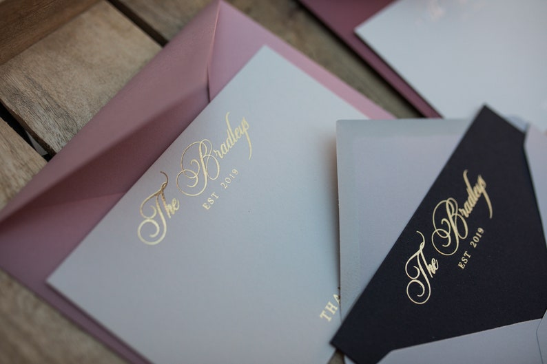 May include: Two envelopes with a light gray and black background. The envelopes have a gold foil design with the text "The Bradley Est 2019".