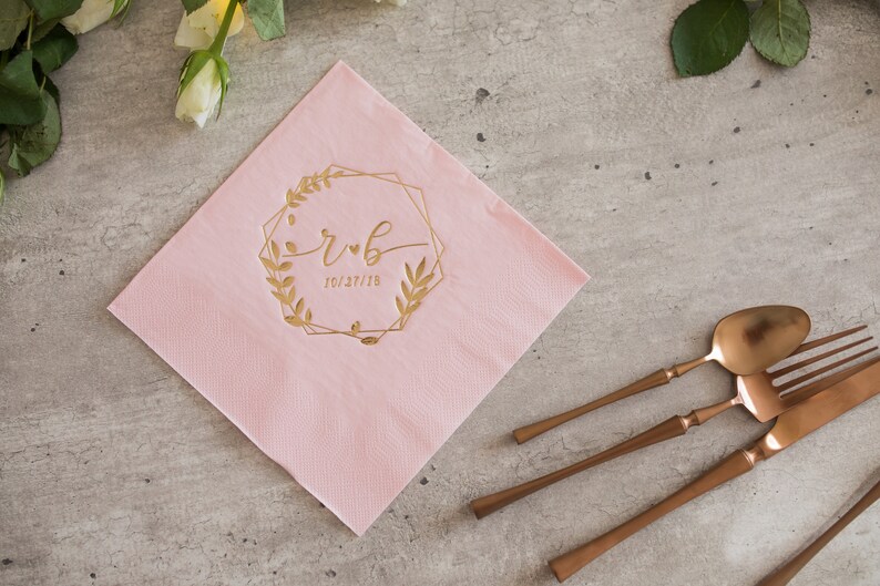Pu&ograve; includere: Tovagliolo di carta rosa con una cornice geometrica dorata e un motivo floreale. La cornice include le iniziali "r & b" e la data "10.27.18".